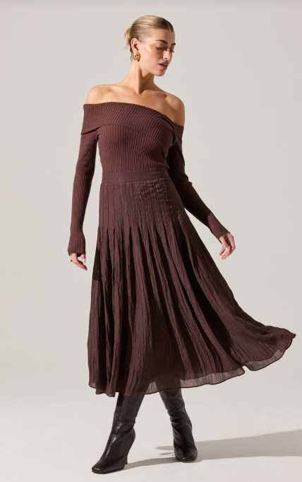 Woman wearing a brown off-shoulder dress with long sleeves on a plain background