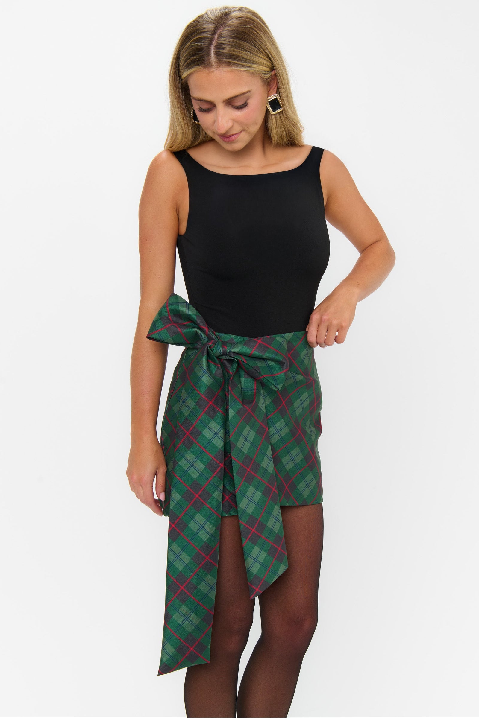 Woman wearing a black top and green plaid skirt on a white background