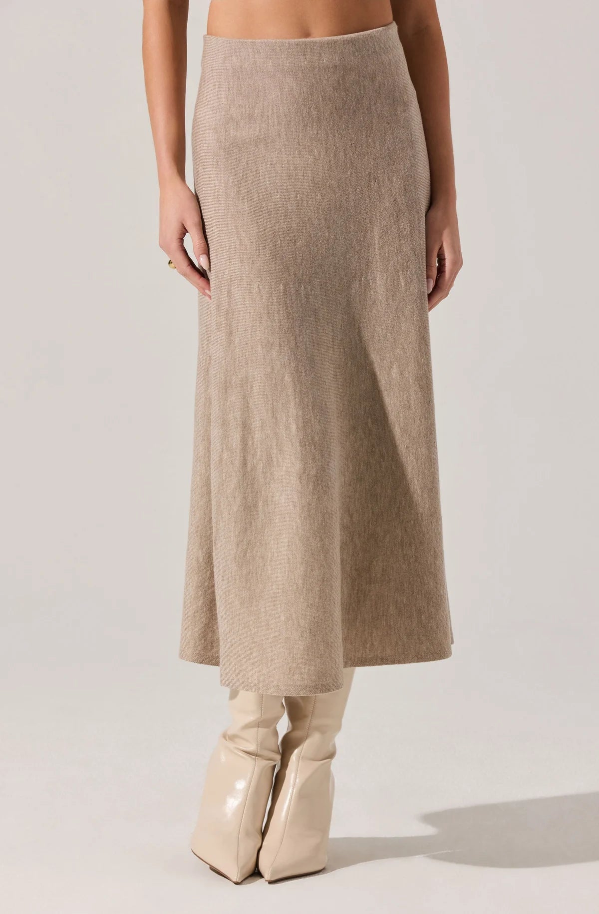 Woman wearing a beige sleeveless dress with a belt against a wooden wall.