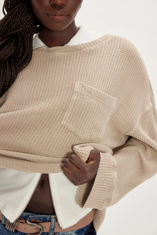 Person wearing a beige knitted poncho with a white shirt underneath on a plain background