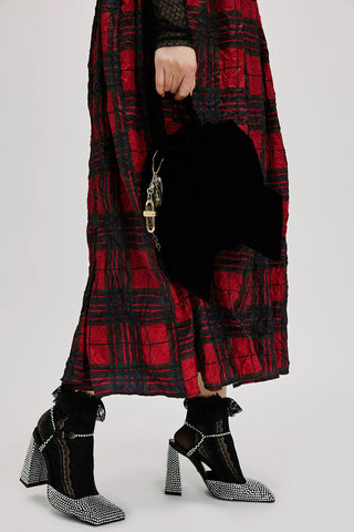 Person wearing a red and black plaid coat with black high-heeled shoes on a plain background