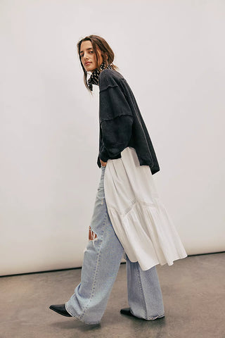 Person wearing a black jacket, white dress, and light blue jeans against a plain background