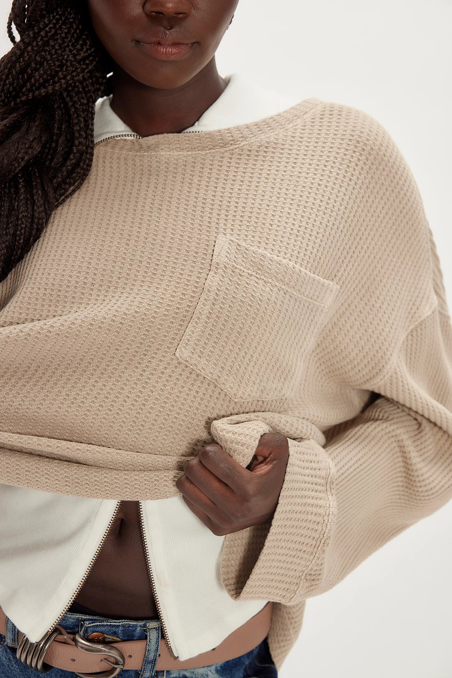 Person wearing a beige knitted poncho with a white shirt underneath on a plain background