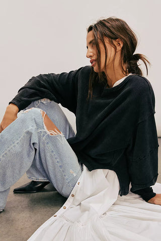 Woman sitting on a white surface wearing a black oversized sweatshirt and light blue jeans.