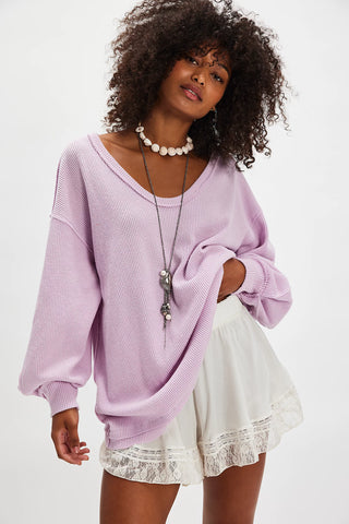 Woman wearing a light purple sweater and white lace skirt on a plain background