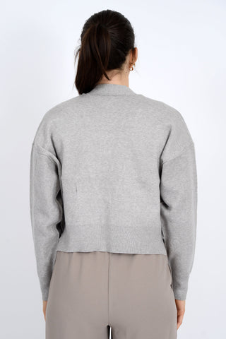 Person wearing a gray sweater and beige pants on a white background