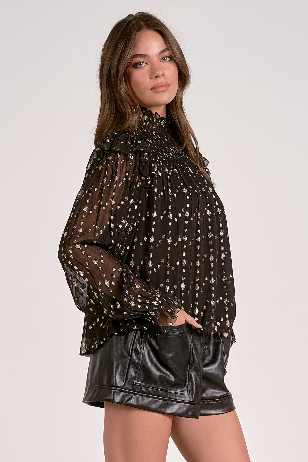 Woman wearing a black polka dot blouse and black leather shorts on a white background