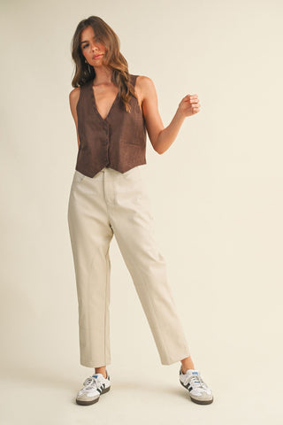 Woman wearing a brown sleeveless top and beige pants on a plain background