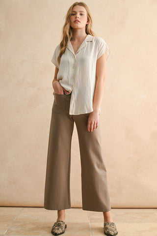 Woman wearing a white blouse and brown pants against a beige background