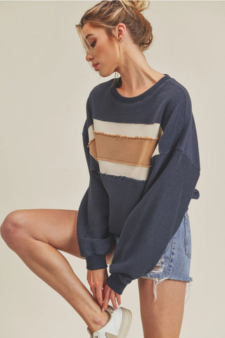 Woman wearing a navy sweater with beige and brown stripes and denim shorts on a beige background