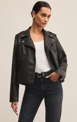 Woman wearing a black leather jacket over a white top and dark jeans on a beige background