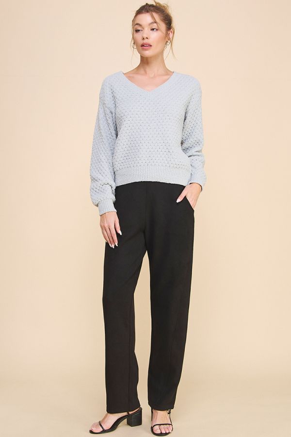 Woman wearing a light blue patterned sweater and black pants on a beige background