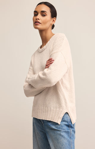 Woman wearing a beige sweater and blue jeans against a plain background
