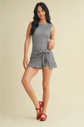 Woman wearing a black and white checkered dress with red shoes on a beige background