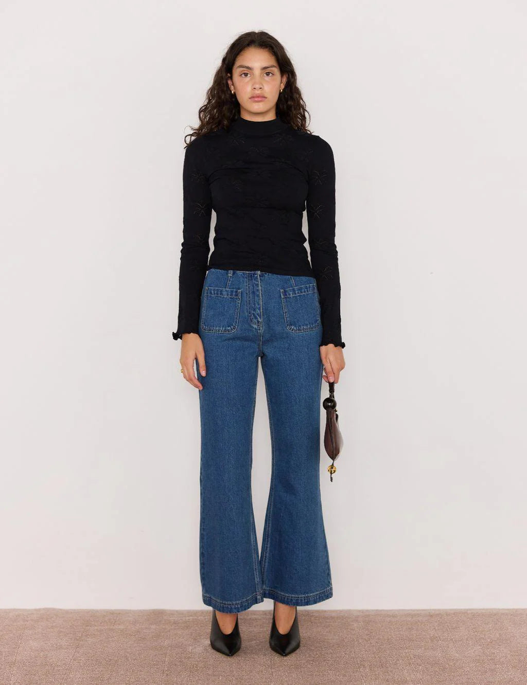 Woman wearing a black turtleneck and blue jeans against a plain background