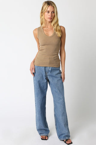 Woman wearing a beige tank top and blue jeans on a white background