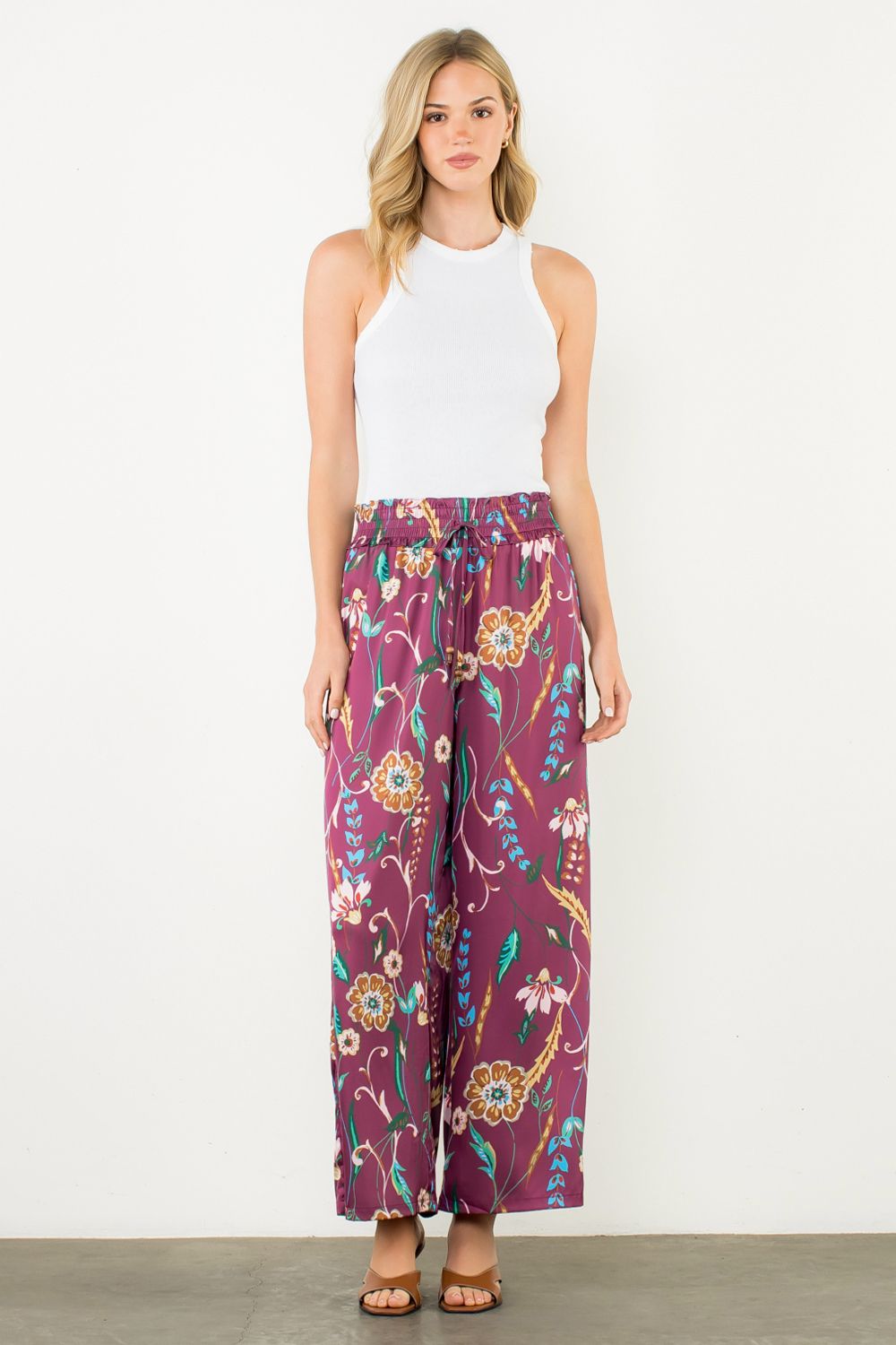 Woman wearing a white sleeveless top and purple floral pants on a white background