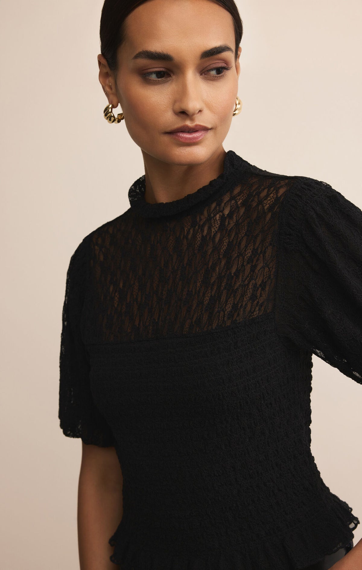 Woman wearing a black top with sheer pattern against a beige background