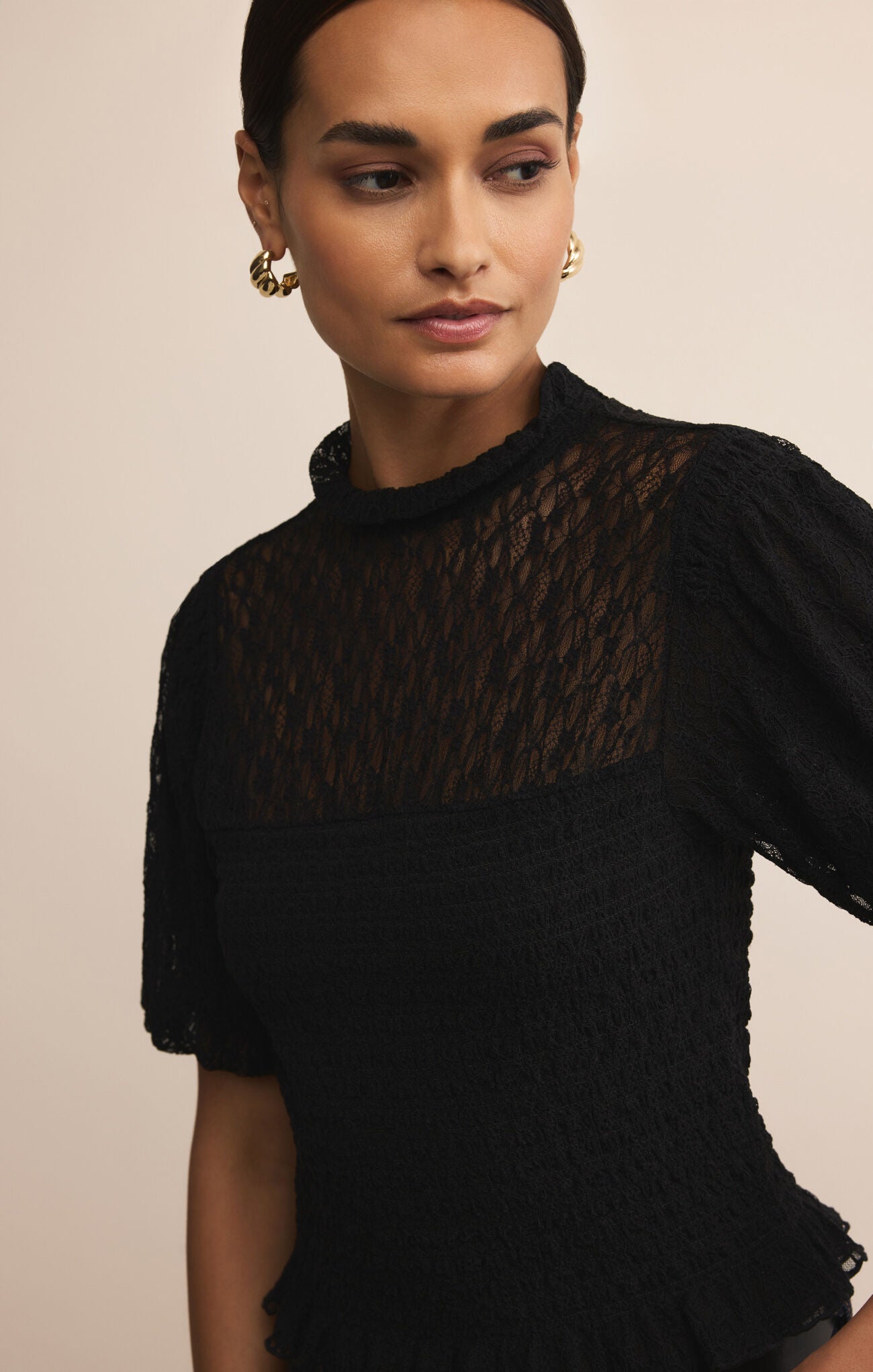 Woman wearing a black top with sheer pattern against a beige background