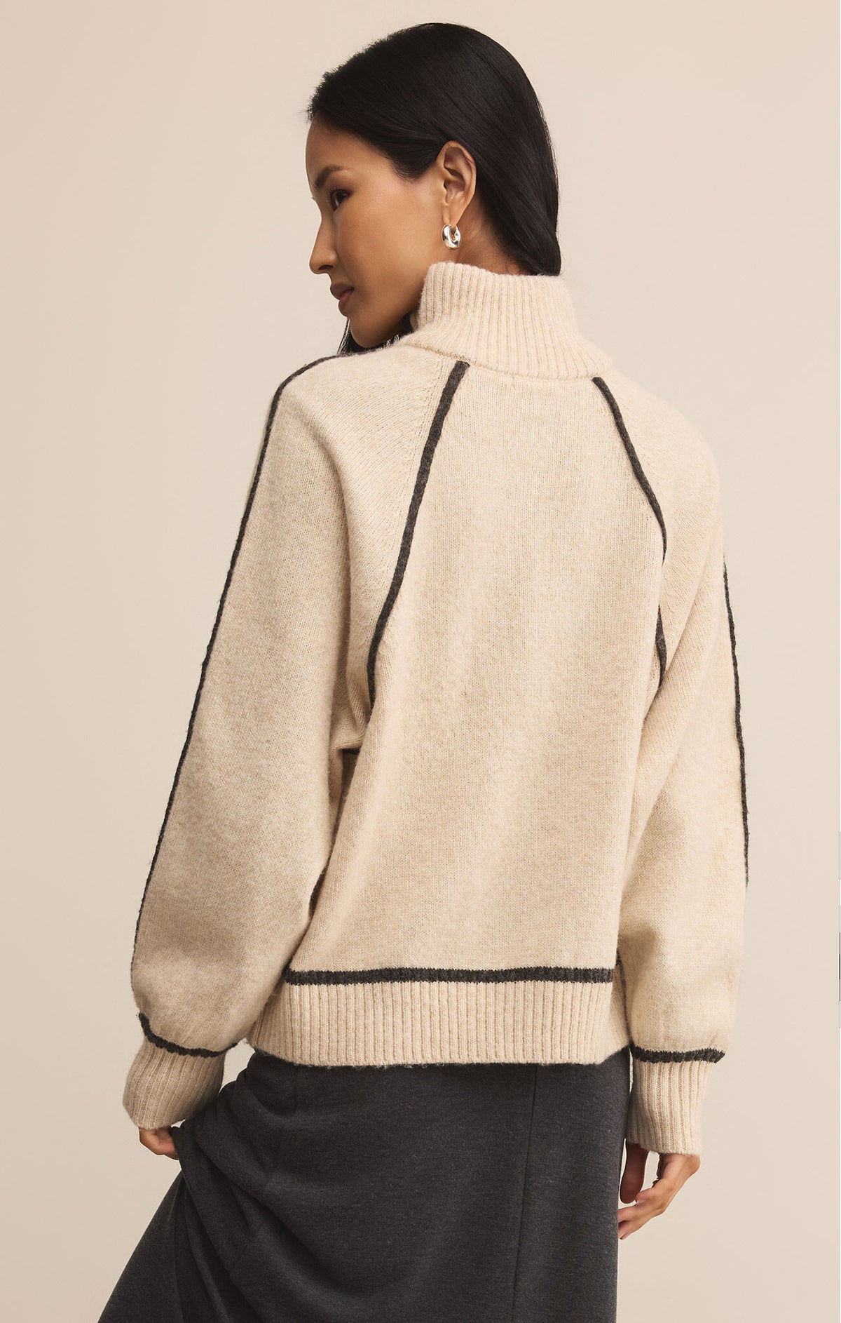 Woman wearing a beige sweater with black trim on a beige background