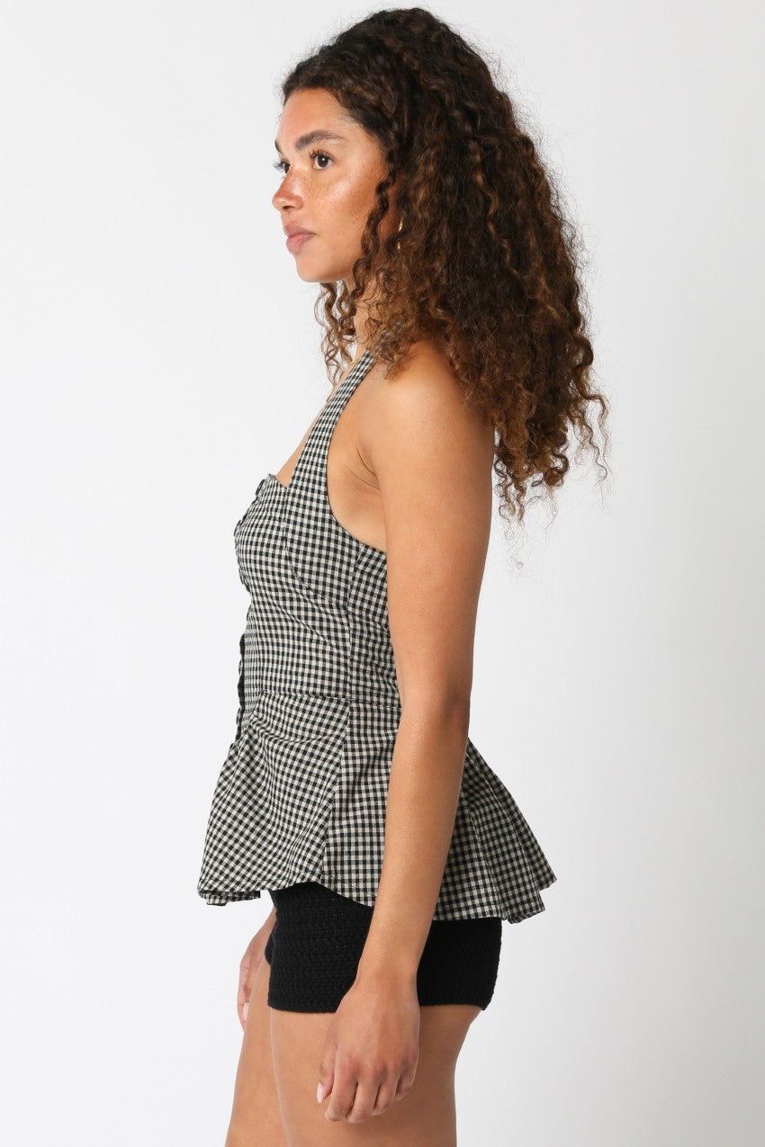 Woman wearing a black and white checkered halter top with buttons on a plain background