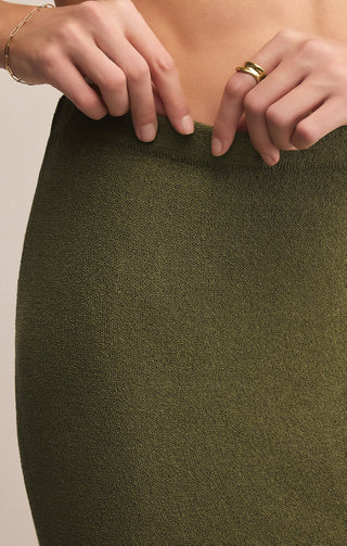 Close-up of a person wearing an olive green skirt with hands adjusting the fabric.