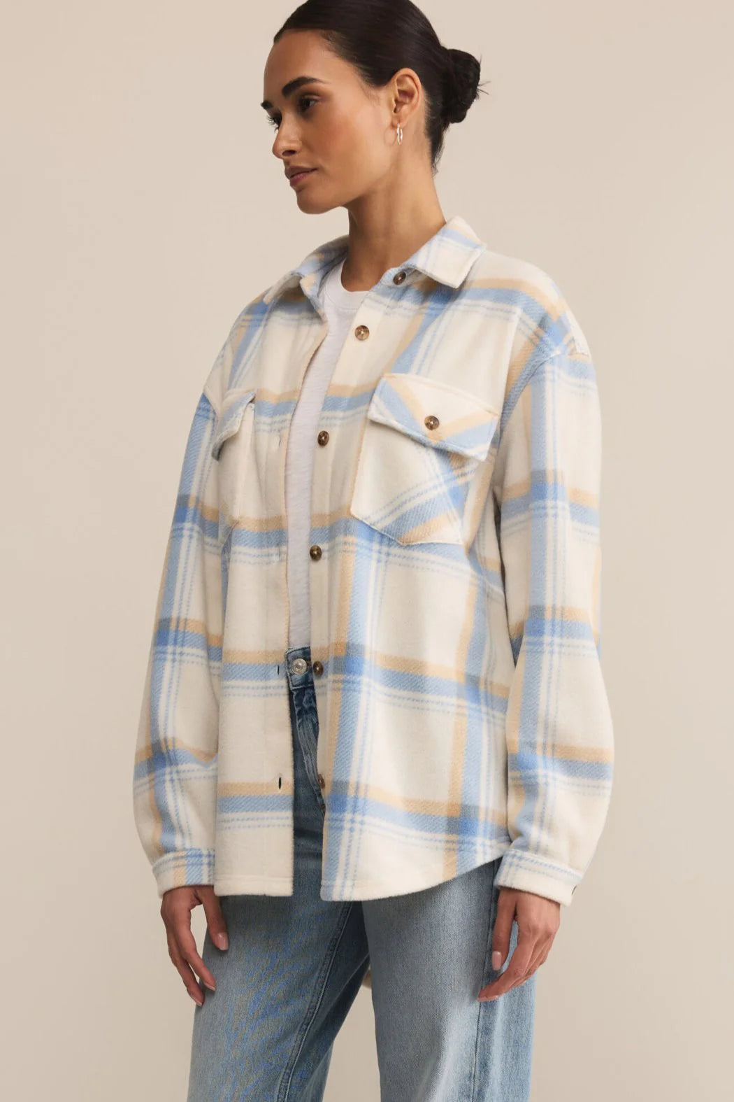 Woman wearing a plaid shirt over a white top and jeans on a beige background