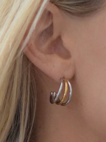 Close-up of a person wearing a silver and gold hoop earring.