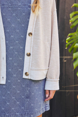 Person wearing a beige jacket over a blue denim dress with white patterns.