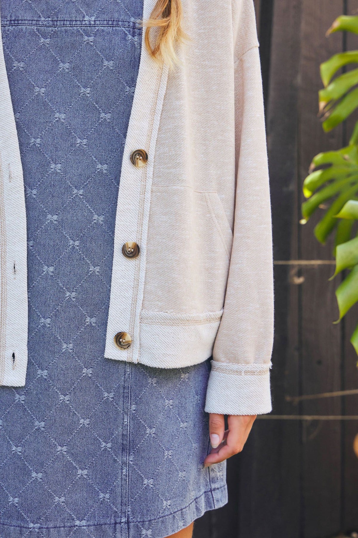 Person wearing a beige jacket over a blue denim dress with white patterns.