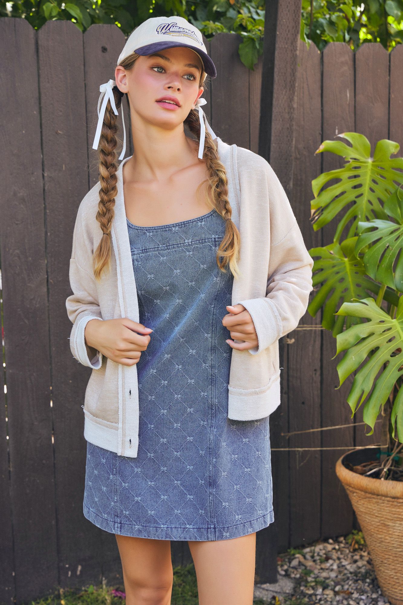 Woman with braided hair wearing a denim dress and beige cardigan outdoors.
