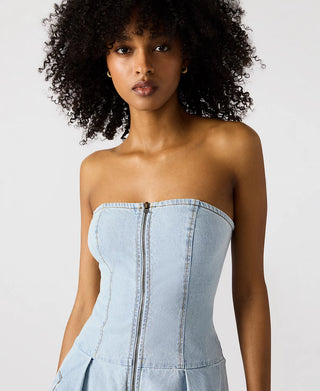 Woman wearing a light blue strapless denim dress against a plain background