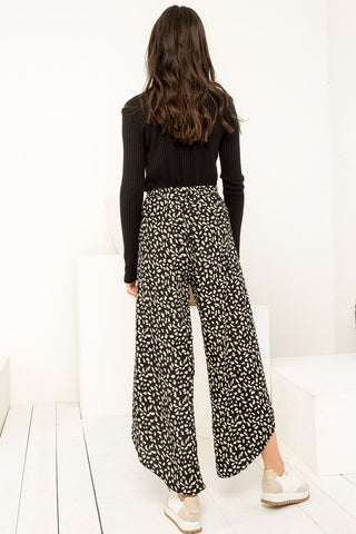 Person wearing black long-sleeve top and patterned wide-leg pants on a white background