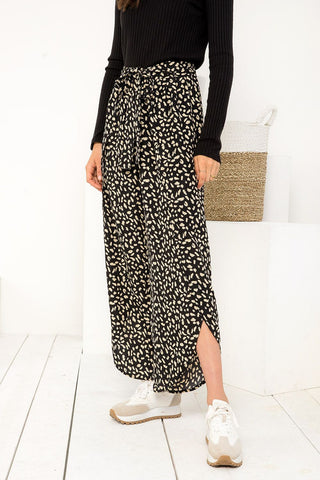 Person wearing a black patterned skirt with white shoes on a white floor.