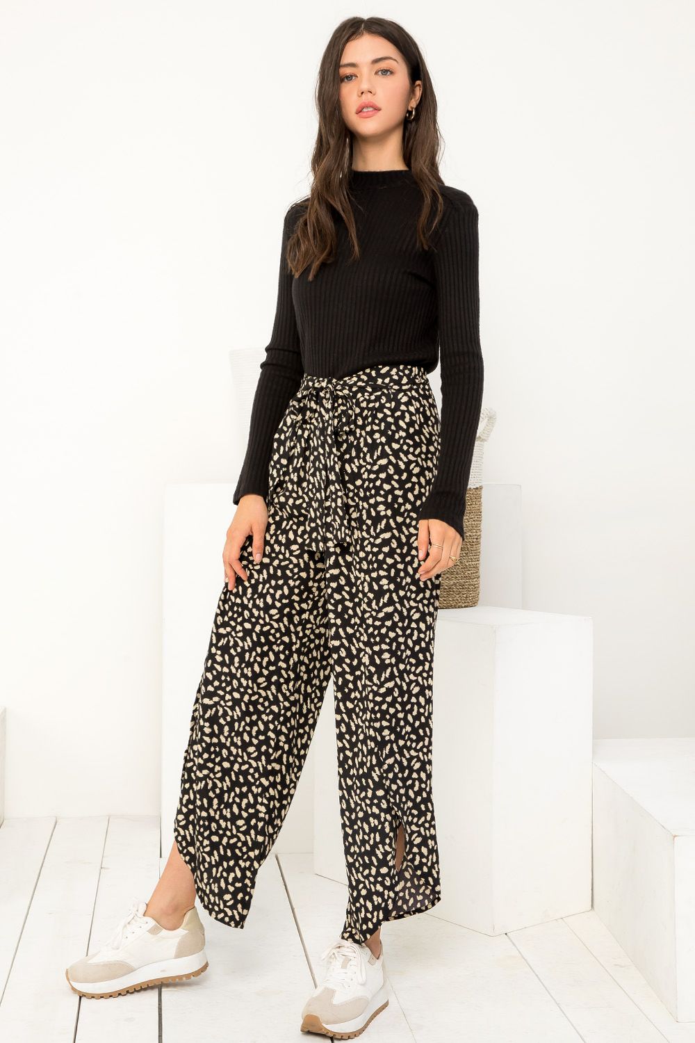 Woman wearing a black long-sleeve top and patterned pants on a white background