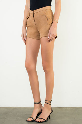 Person wearing tan shorts and black high-heeled sandals on a plain background