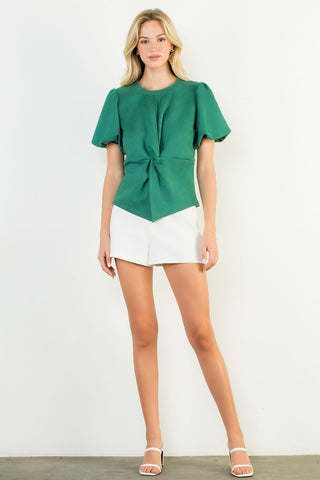 Woman wearing a green top and white shorts on a plain background