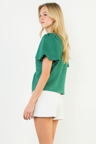 Woman wearing a green blouse and white skirt on a plain background