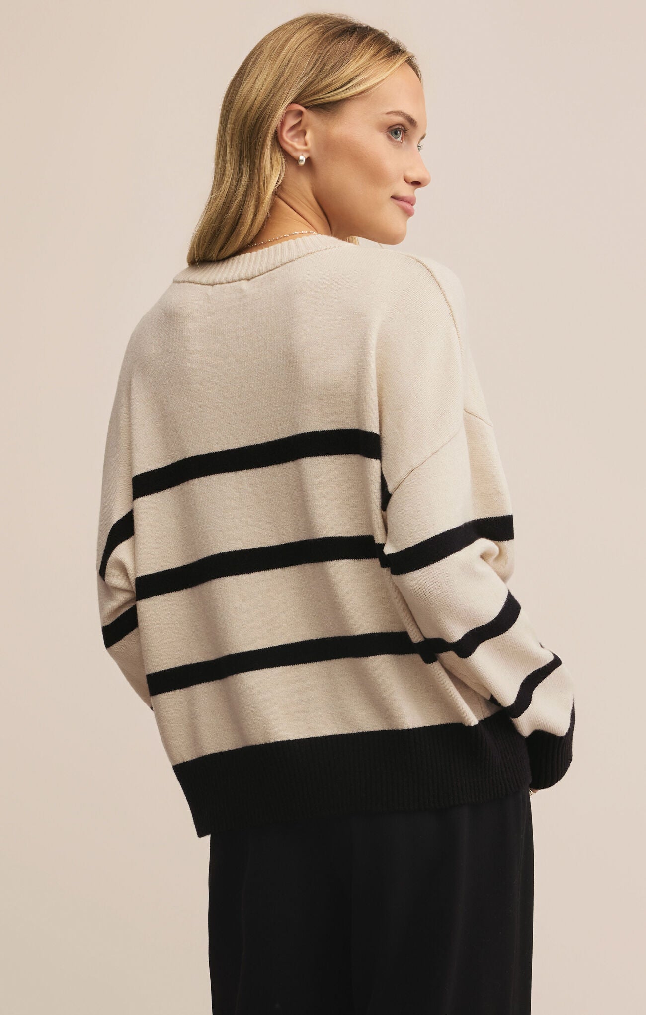 Woman wearing a beige sweater with black stripes on a plain background