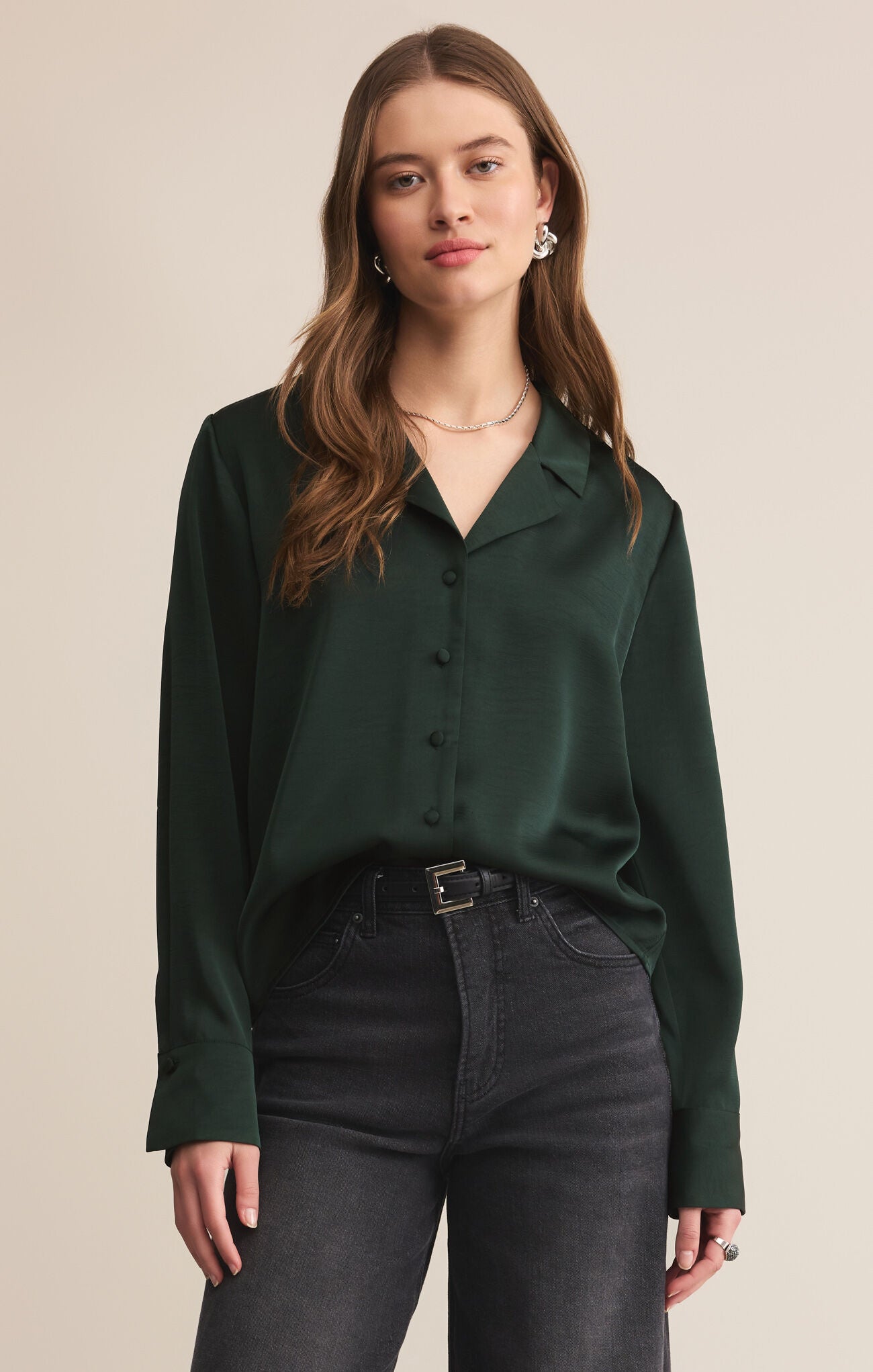 Woman wearing a dark green blouse and black pants against a beige background