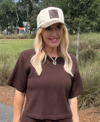 Woman wearing a brown shirt and white cap with leopard print brim outdoors