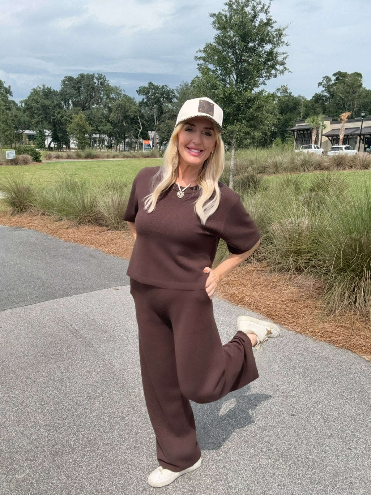 Woman in a brown outfit standing outdoors with greenery in the background