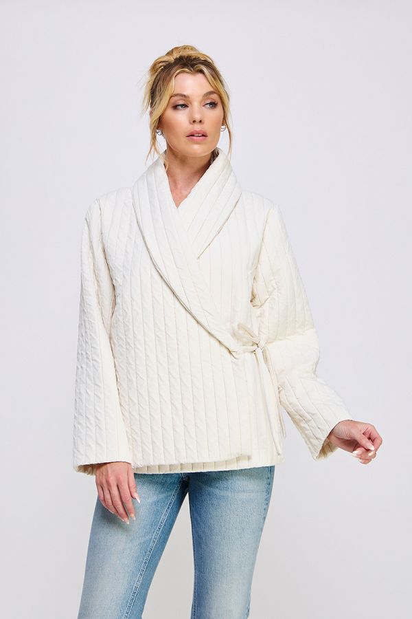 Woman wearing a white ribbed sweater and light blue jeans on a plain background