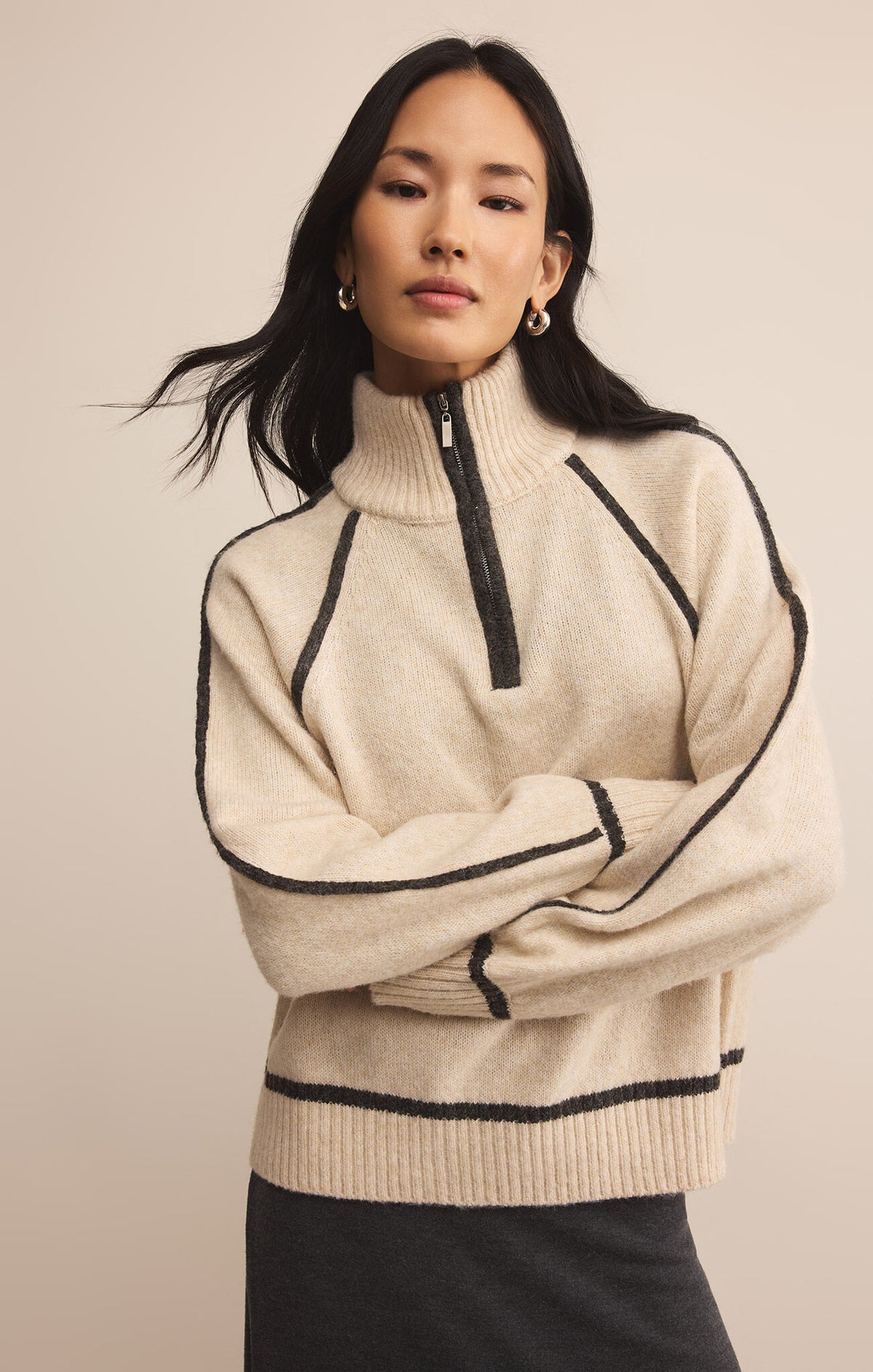 Woman wearing a beige sweater with black accents against a plain background