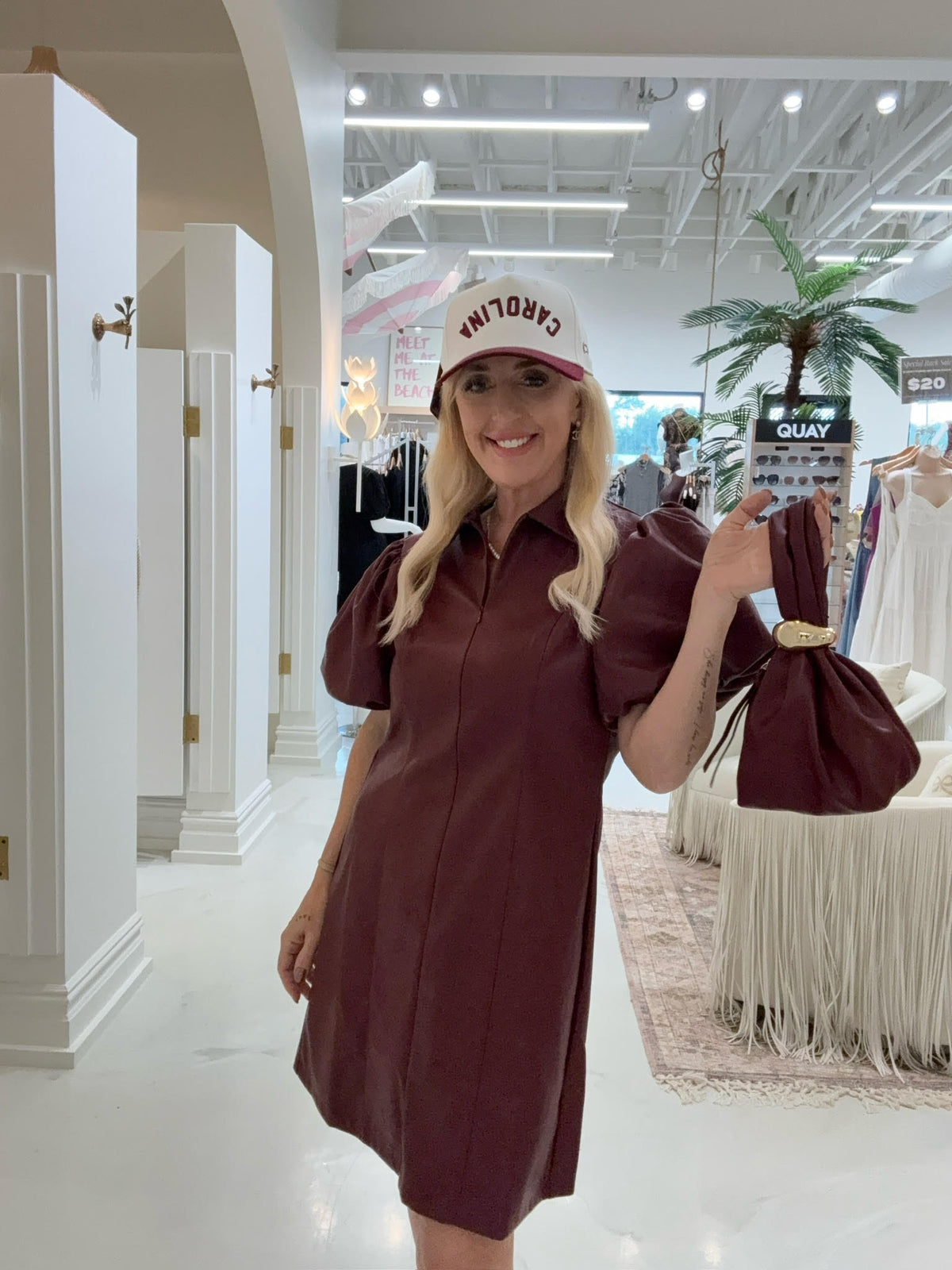 Woman in a maroon dress and white cap holding a phone in a store setting