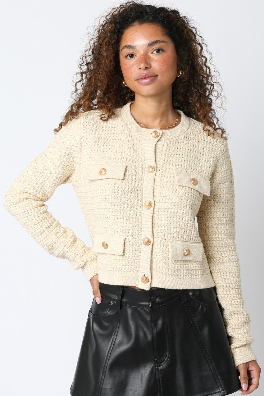 Woman wearing a beige textured jacket with gold buttons on a plain background