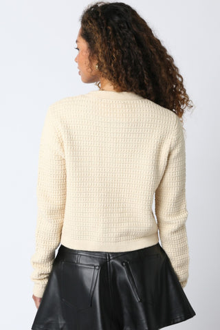 Person wearing a beige textured sweater and black leather skirt on a light gray background