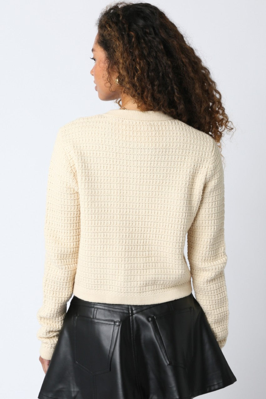 Person wearing a beige textured sweater and black leather skirt on a light gray background