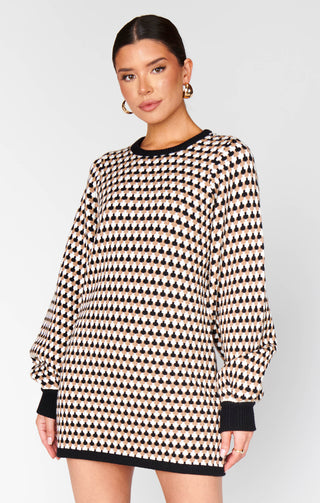 Woman wearing a black and white patterned sweater dress on a plain background