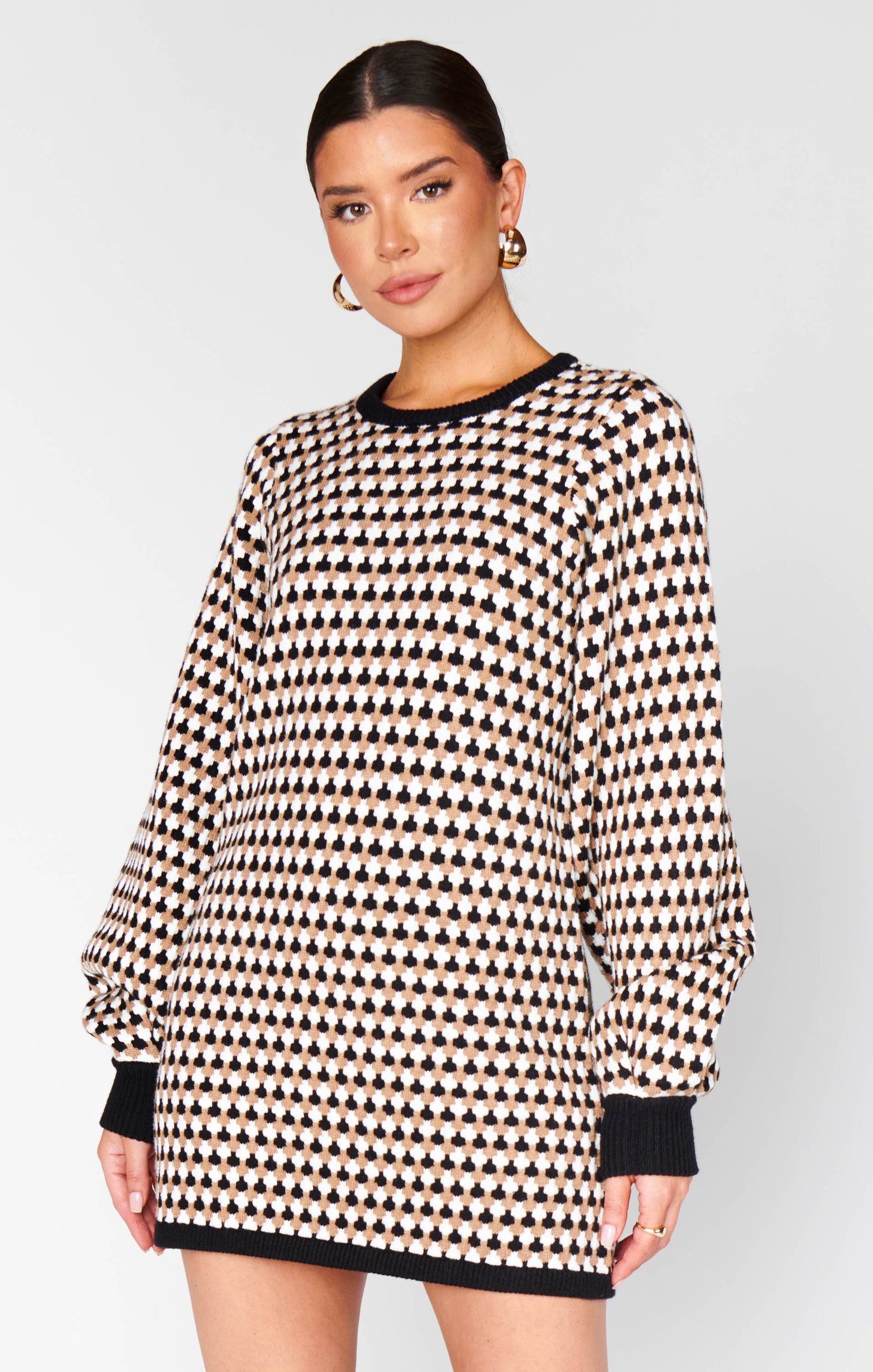 Woman wearing a black and white patterned sweater dress on a plain background